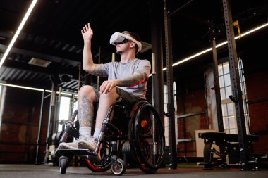 Spor salonunda tekerlekli sandalye kullanan ve AR teknolojisi kullanan genç bir adamın yan görüş portresi.