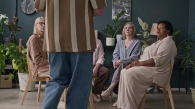 Kafkasyalı üst düzey erkek psikologların, yaşlılar için grup terapisi seanslarını yönetirken, daireler çizerek otururken ve modern ofiste tartışırken yavaş çekimler.