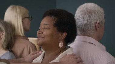 Modern sınıftaki beyaz erkek uzmanla grup terapisinde meditasyon yapan çok ırklı bir grup yaşlı insan.