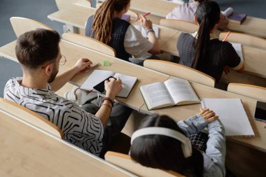 Masada oturan ilgisiz öğrencilerin yüksek açılı görüntüleri ellerinde not defterleri ve cep telefonları ile üniversite dersinde dikkatleri dağıtıyor.