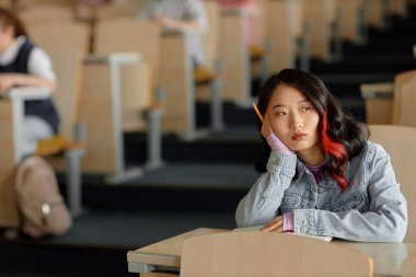 Üniversitede derslere katılırken sırtüstü yan yan yan bakan Asyalı genç kız öğrencinin portresi.