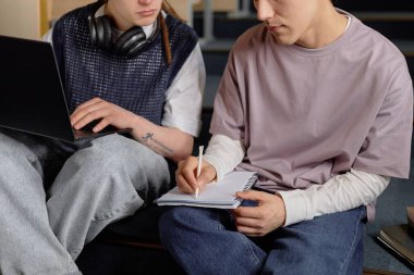 Not defterinde kalemle tanınmayan bir erkek öğrencinin kısa görüntüsü ve erkek sınıf arkadaşı laptopta çalışırken konferans odasında birlikte otururken sınava hazırlanıyor.