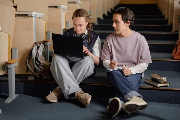 Stock image Full length two young male fellow students surfing net on laptop while sitting together on stairs in lecture hall at university