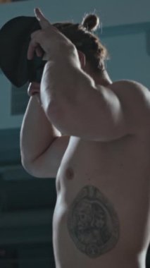 Kafkas erkek yüzücünün dikey pozisyonu. Kaburgasında siyah dövme var. Kapalı havuzda yarışa başlamadan önce yüzme şapkası takıyor.