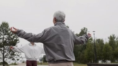 Bulutlu gökyüzünün altında yoga yaparken dua eden elleri ve gözleri kapalı duran üç yaşlı kadının yavaş çekimleri.