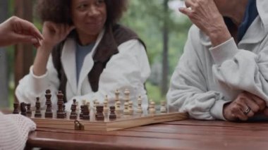 Yağmurlu bir günde parkta satranç oynarken etnik çeşitliliğe sahip üç olgun bayan arkadaş konuşuyor.
