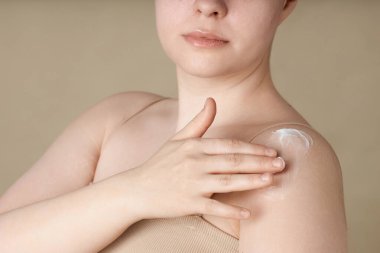 Yumuşak, soluk tenli, omuzlarına krem süren genç bir kadının minimum yakın çekimi.