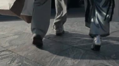 Pahalı siyah arabaya doğru yürüyen, Asyalı sürücülere kese kağıdı veren ve içeri giren ünlü çiftin arka görüntüsü.