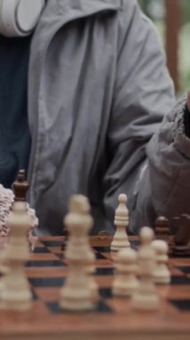 Tanımlanamayan son sınıf arkadaşlarının parktaki ahşap masada satranç oynayarak boş zamanlarını geçirdikleri dikey görüntüler.