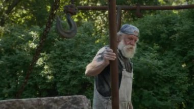 Kafkas sakallı yaşlı bir adamın dışarıda taş malzemelerle çalışırken, heykel yaparken ve el işi yaparken orta boy fotoğrafı.