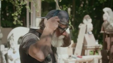 Profesyonel beyaz erkek heykeltraşın bahçede taşla çalışırken güvenlik kulaklığı taktığı orta boy bir fotoğraf.