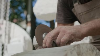 Uzun gri sakallı, konsantre olmuş yetişkin erkek heykeltraşın iş yerindeki açı öğütücüsünü kullanması.