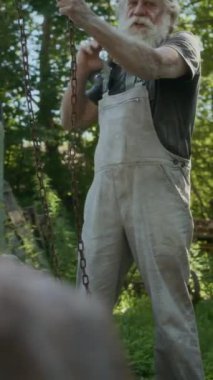 Kafkasyalı yaşlı bir adamın dışarı taştan ağır bir parça taşıdığı için zincirlerini çekerken dikey çekimi.