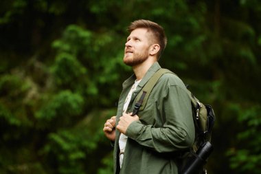 Zengin ormanlarında sırt çantasıyla gezen bir adam. Sakal ve günlük kıyafet, yeşilliğin ortasında duran bu doğa meraklısının engebeli dış görünüşünü güçlendirir.