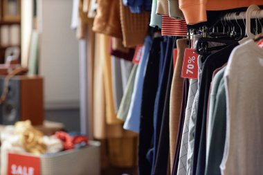 İkinci el dükkanında ya da hayır kurumunda satılık indirimli etiketle askıda asılı duran ikinci el kıyafetlerin arkaplan fotoğrafı.