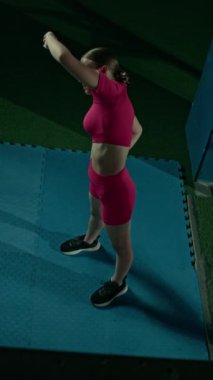 Pembe aktif giyimli beyaz kızın antrenman sırasında spor salonunda ısınırken yan eğildiği dik açılı tam kare.