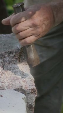 Çekiç ve keski kullanan tanınmayan profesyonel zanaatkârın dikey ve yavaş çekimleri açık havada doğal taşları oyuyor.