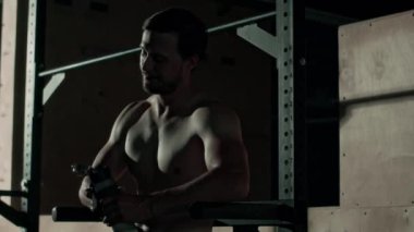 Gömleksiz, formalı genç adam, spor salonunda, gölgeli içme suyunda, paralel barda duruyor ve yorucu spor eğitiminden sonra terini siliyor.