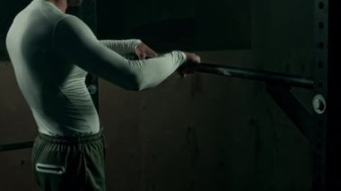 Güçlü beyaz erkek sporcu spor salonunda ön kol egzersizi yapıyor, iki eliyle barı kavrıyor ve vücudunu tamamen genişletiyor.