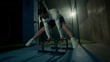 Beyaz tenli, sağlıklı vücutlu ve güçlü kolları olan genç bir sporcu. Koyu renk çatı katı tarzı spor salonunun parmaklıklarında amuda kalkıyor.