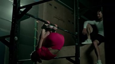 Siyah spor stüdyosunda erkek antrenörle jimnastik yaparken, barın arkasında egzersiz yapan beyaz bir kadının düşük pozu.
