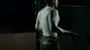Beyaz, uzun kollu sıkıştırma tişörtlü beyaz bir adamın karanlık spor salonundaki düz olmayan barın üzerinde düz bir planche performans sergiliyor.