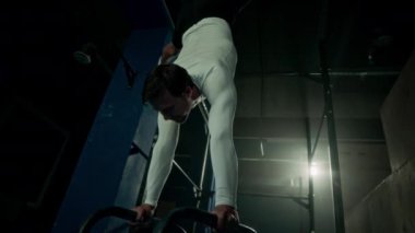 Beyaz tenli genç sporcu, karanlık çatı katı tarzı spor salonlarında jimnastik tesisleriyle antrenman yaparken barın üstünde sert durduğunu gösteriyor.