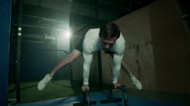 Güçlü kaslı kolları ve vücudu olan atletik bir adam, koyu renk çatı katı tarzı spor salonunda antrenman yaparken ileri düzey bir planche sergiliyor.