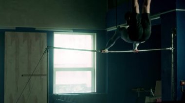 Beyaz tenli atletik adam jimnastik barında akrobatik dublörlük yapıyor.