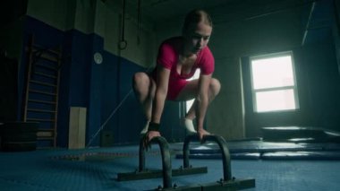 Beyaz kadın sporcu kadın sporcu. Paralel barlarda jimnastik öğeleri gösteriyor. Koyu renk spor salonunda, tesislerle antrenman yaparken.