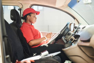 Kırmızı üniformalı genç Afrikalı bir kadın teslimat kamyonetinde dijital tablet okuyor iş performansında verimliliği ve doğruluğu artırıyor
