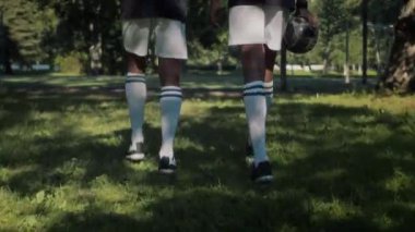 Kamu parkında yeşil çimlerde birlikte sahaya çıkarken spor üniforması giyen iki Afrikalı Amerikalı genç futbolcunun arka plan çekimini kaldırın.