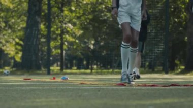 İki Afrikalı Amerikalı genç futbolcunun futbol antrenmanı sırasında sahada beyaz erkek koçla çim üzerinde merdiven gibi düz merdiven kullanarak hız ve çeviklik testi yapmasının tam karesi.