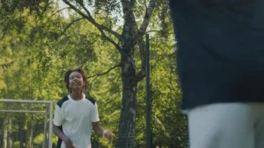 Genç Afrikalı Amerikalı erkek futbolcunun güneşli bir günde parkta arkadaşı ve koçuyla antrenman yaparken kafasıyla topa vurduğu orta boy bir fotoğraf.