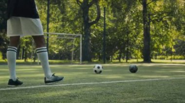 Afrika kökenli Amerikalı bir gencin parkta çimenlik alanda antrenman yaparken futbol toplarını ağda tekmelemek için antrenman yaptığı sahne.