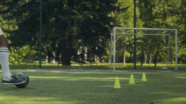 Genç Afrikalı Amerikalı erkek futbolcu kalede topa vuruyor ve koçla çimenlik alanda antrenman yaparken gol atıyor.
