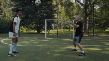 Profesyonel beyaz erkek futbol antrenörü Afrika kökenli Amerikan genine yaz aylarında parkta antrenman yaparken kafasıyla topa vurmasını öğretiyor.