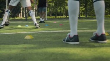 İki genç Afrikalı Amerikalı çocuk, beyaz erkek koçla gündüz vakti çimenlik alanda futbol antrenmanında.