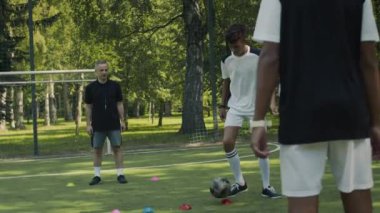 İki genç Afrikalı Amerikalı oyuncuyla Kafkas antrenman koçunun çimenli sahada futbol antrenmanının tam çekimi.