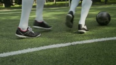 Beyaz uzun çoraplar ve spor ayakkabılar giyen, çimenli arazide futbol oynayan, tanınmayan iki çocuğun alçak kesimi.