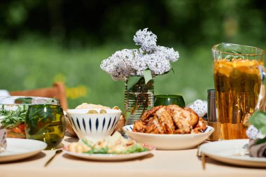 Dışarıdaki masa, çeşitli yeni hazırlanmış yemek ve içeceklerle güzelce hazırlandı. Bir buket çiçek yemek deneyimine zarafet katar.