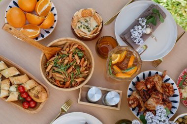 Makarna, tavuk, çeşitli ekmek, taze meyve ve içecek de dahil olmak üzere Akdeniz yemeklerinin bulunduğu zarif bir yemek düzeninin yukarıdan aşağı görüntüsü.