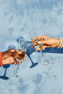 Close-up of two hands clinking champagne glasses creating celebratory moment against blue background suggesting elegance and sophistication clipart