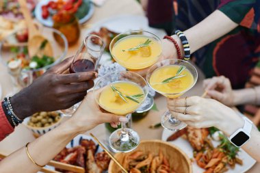 Çok ırklı arkadaşlar kokteyl ve şarap kadehleri kaldırıyor, arkadaşlığı kutluyor ve açık havada iştah açıcı yemekler ve canlı bir atmosferle çevrili yiyeceklerin tadını çıkarıyor.