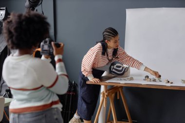 Saçı örgülü siyah genç bir kadının portresi fotoğrafçı asistanı olarak stüdyo fotokopi odasında ürün fotoshoot için hazırlanıyor.