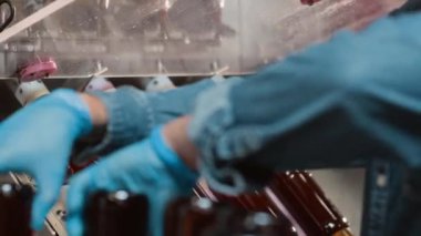 Kahve şişelerini bira ya da elma suyuyla doldurmak için doldurma makinesi kullanan tanınmamış bira fabrikası işçisinin kırpılmış görüntüsü.