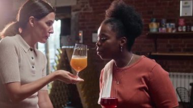 Kırmızı tuğlalı barda elma suyu içen iki farklı kadının orta boy fotoğrafı.