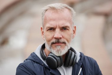 Kameraya bakarken kulaklıklı, kıdemli, beyaz saçlı, gülümseyen adama yaklaş.