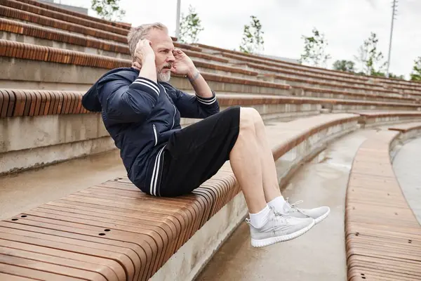 stock image Side view of athletic elderly man in sportswear doing crunches on bench strengthening ab muscles during everyday workout at city park, copy space