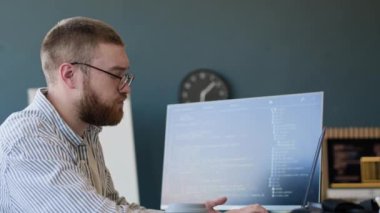 Laptop 'ta kod yazan ve masaüstü bilgisayarında ve defterde verileri kontrol eden Kafkasyalı genç programcının yan görünümü